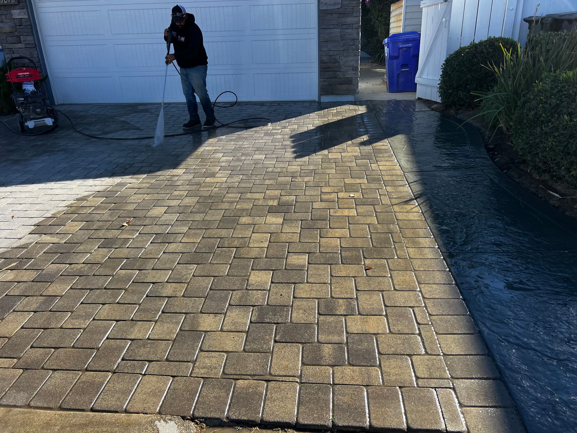A man is cleaning a brick driveway with a high pressure washer.