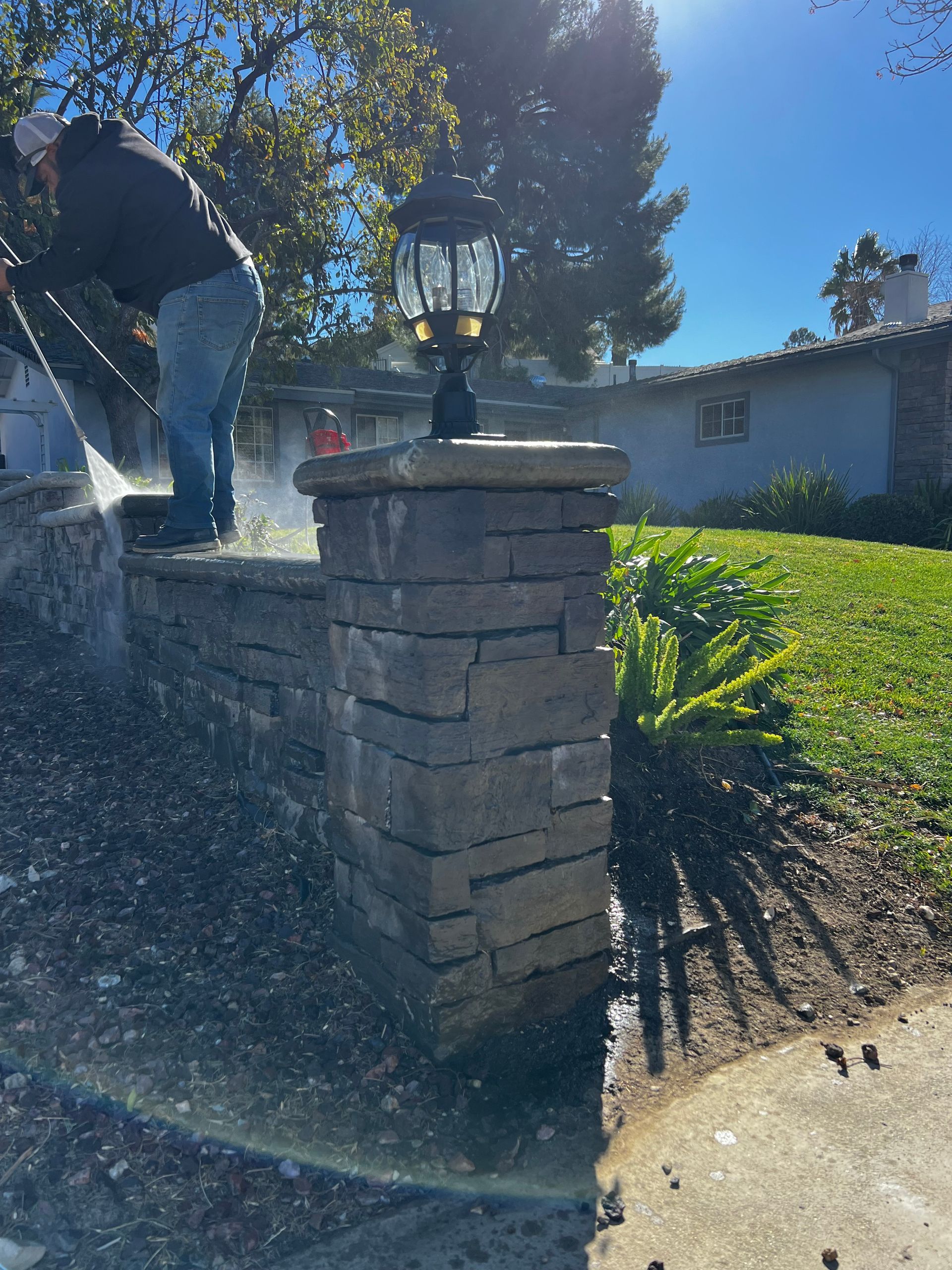A man is cleaning a brick wall in front of a house.