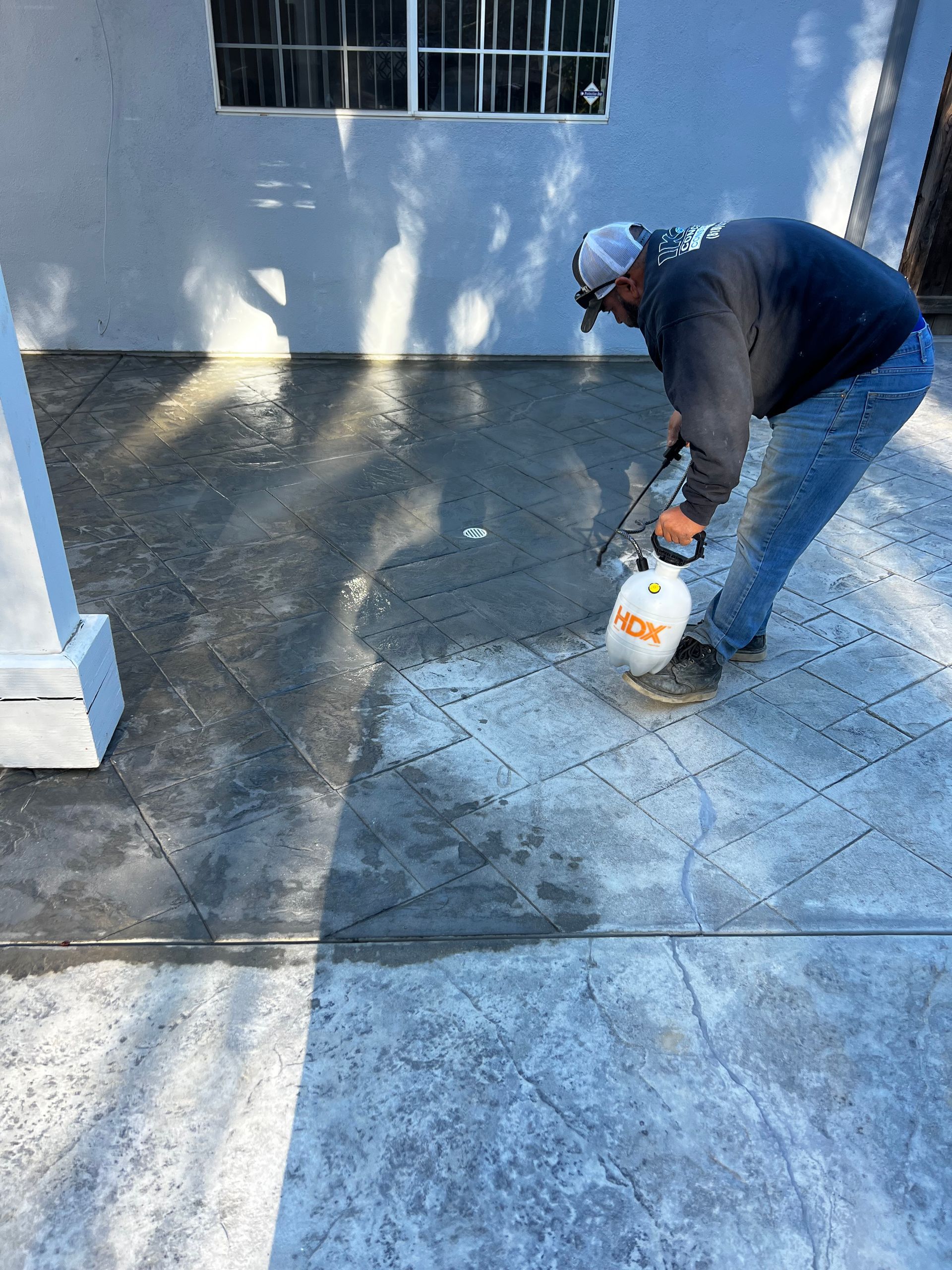A man is spraying concrete on a patio with a sprayer.