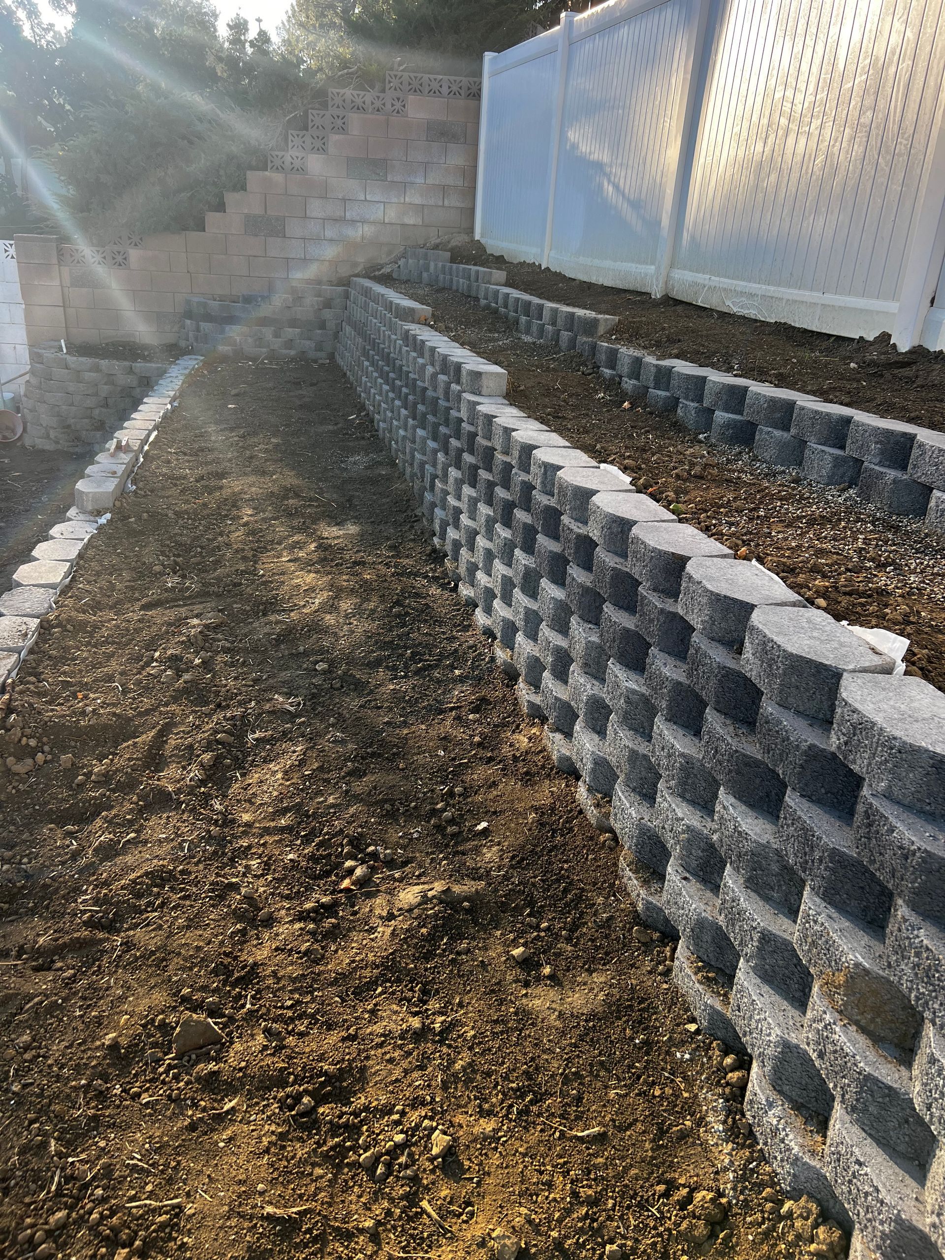A brick wall is sitting on top of a dirt hill next to a white fence.