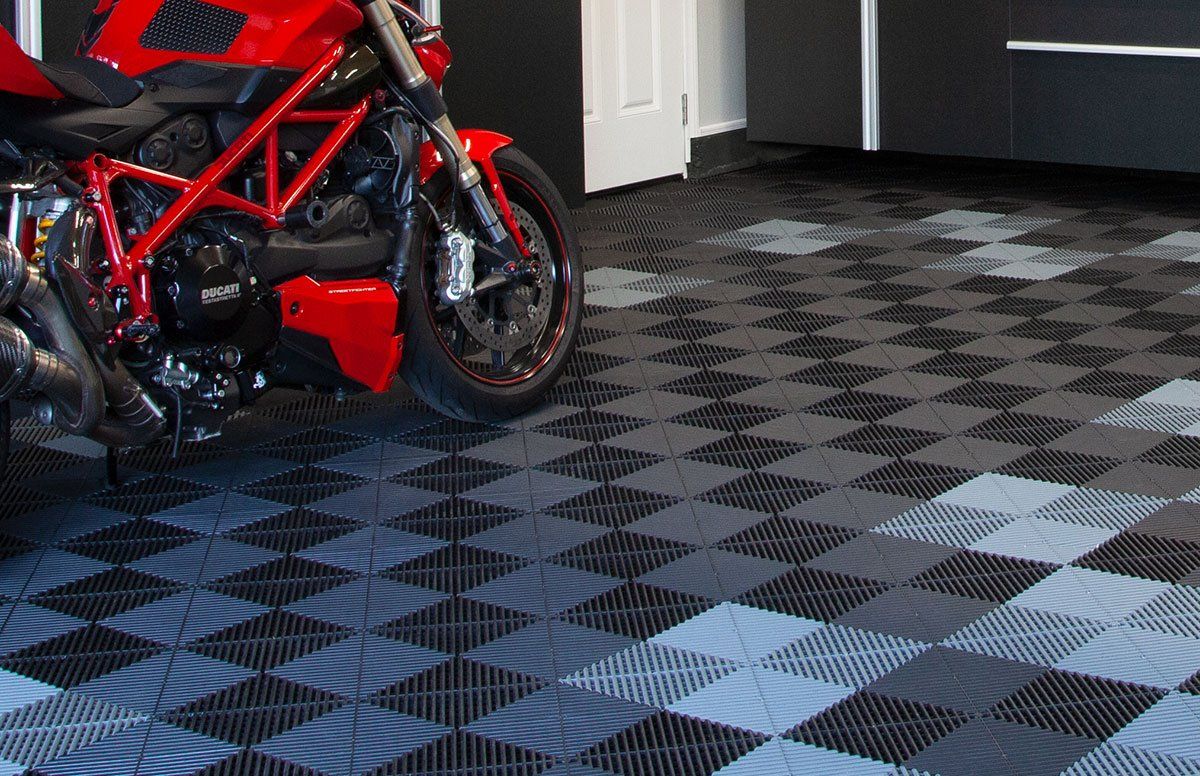a red motorcycle is parked on a checkered swisstrax tile floor in a garage .
