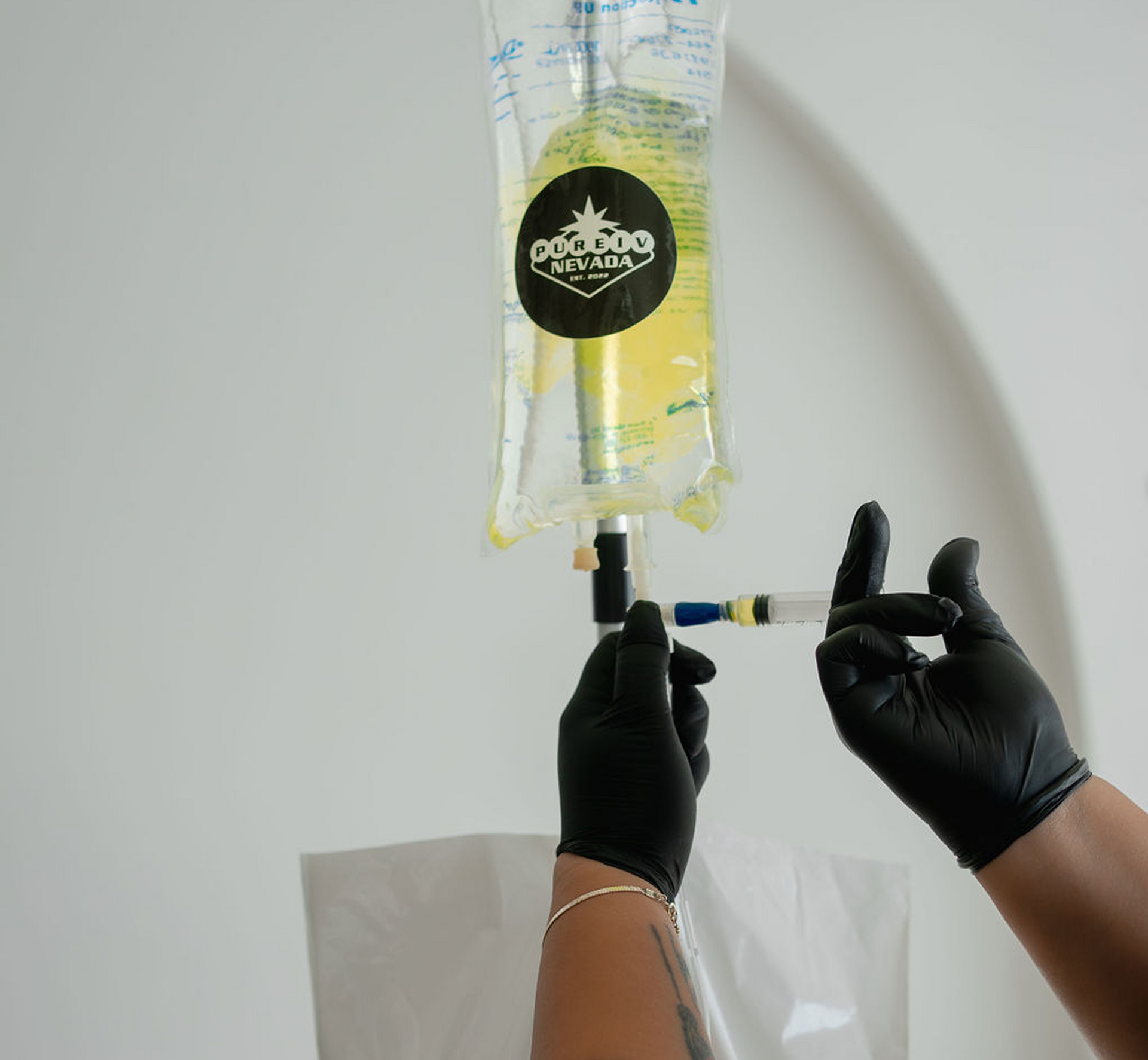 A person wearing black gloves is holding a syringe and a bag of liquid.