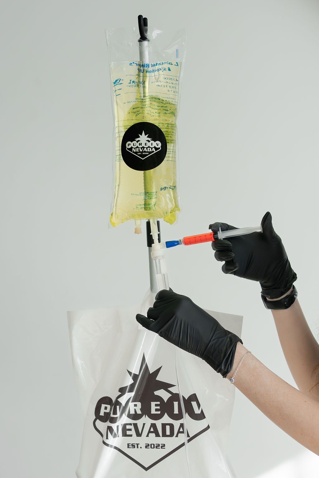 A person is holding a syringe next to a bag of liquid.