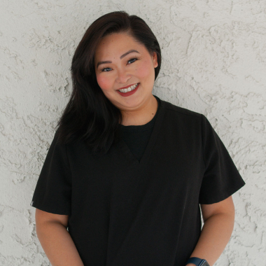 A woman in a black shirt is smiling in front of a white wall