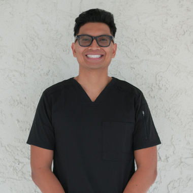 A man wearing glasses and a black scrub top smiles for the camera