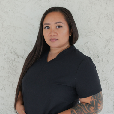 A woman with a tattoo on her arm is wearing a black scrub top.