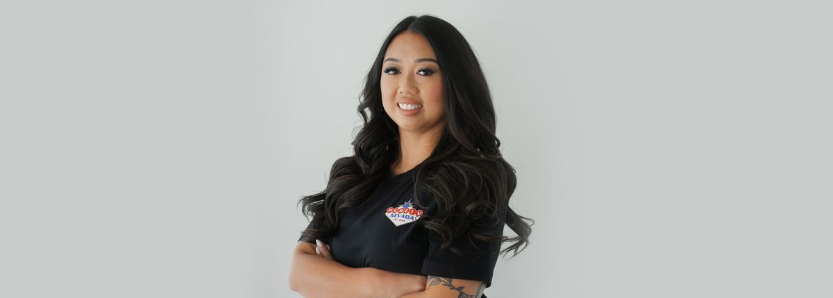 A woman with long hair is standing with her arms crossed and smiling.