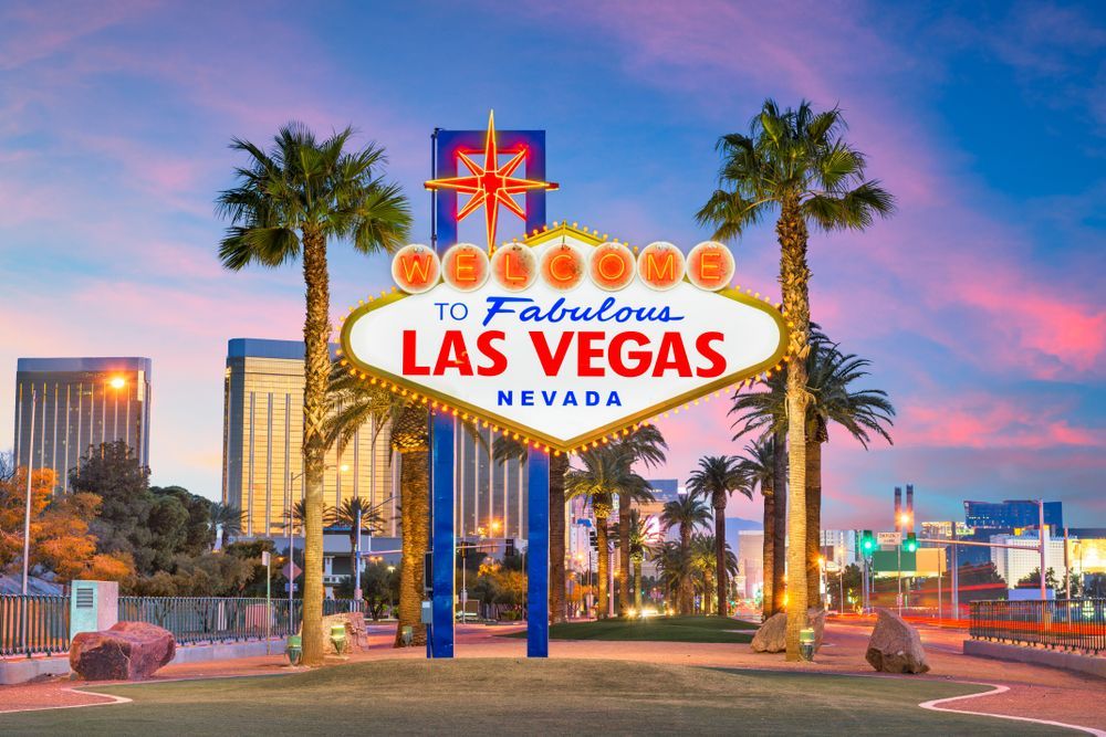 The las vegas sign is surrounded by palm trees and buildings.