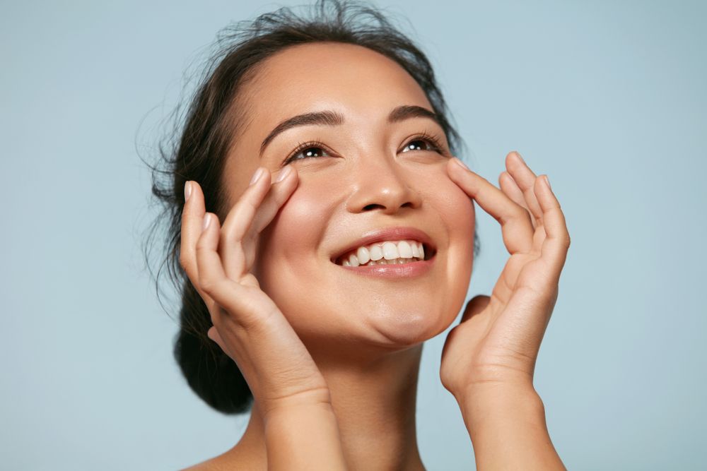 A woman is smiling and touching her face with her hands.