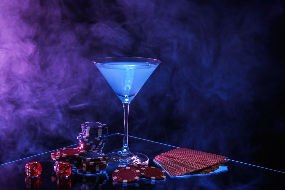 A martini glass filled with blue liquid next to a pile of poker chips and dice.