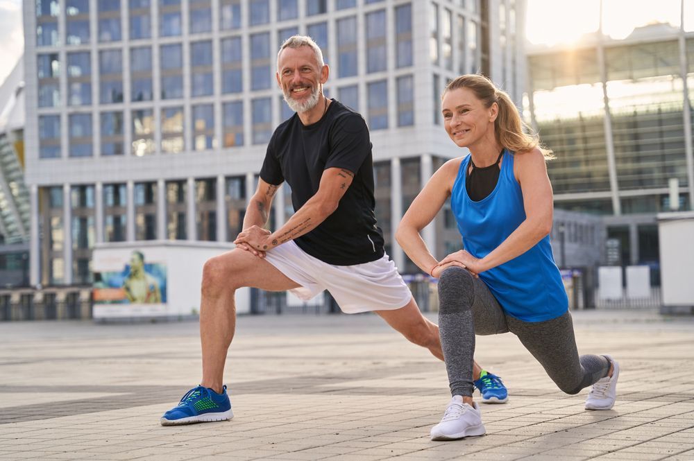 A man and a woman are stretching their legs in front of a building.