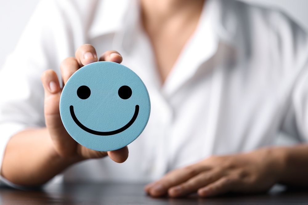 A woman is holding a blue smiley face in her hand.