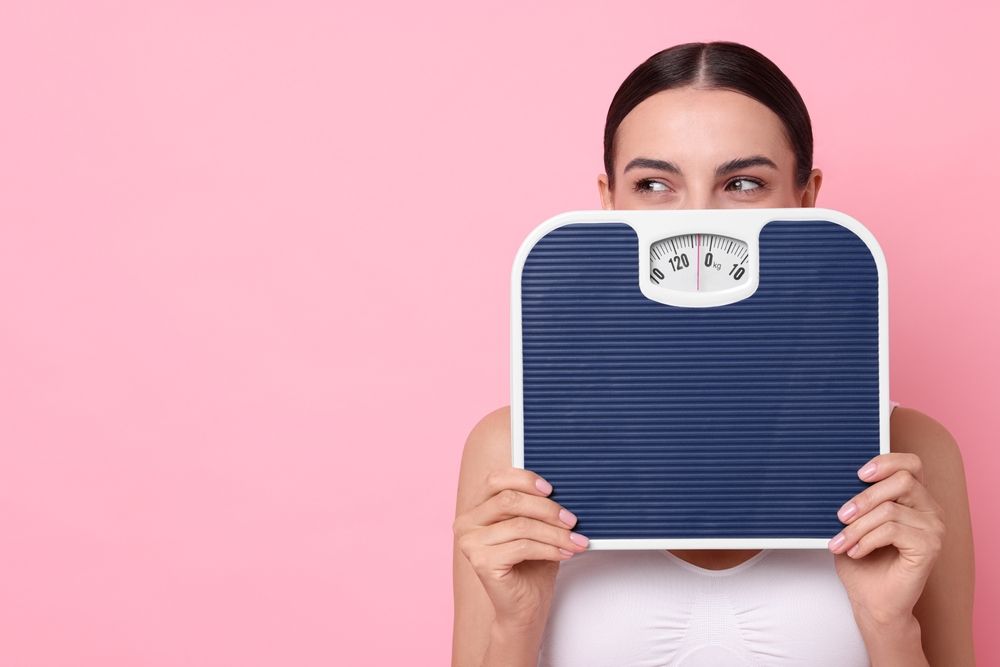 A woman is holding a scale in front of her face.