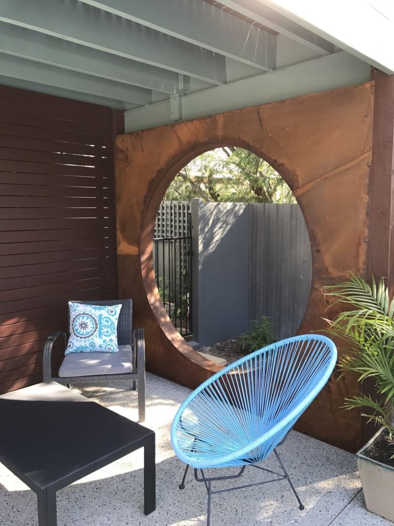 A blue chair is sitting in front of a round window on a patio.