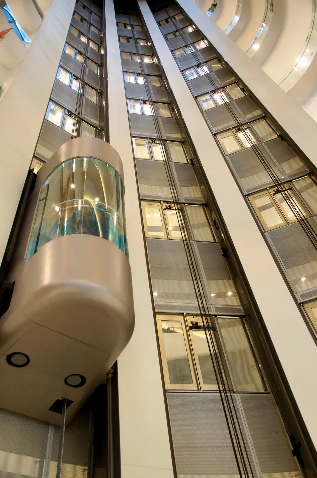 A glass elevator ascends a tall building, traveling past multiple floors with windows.