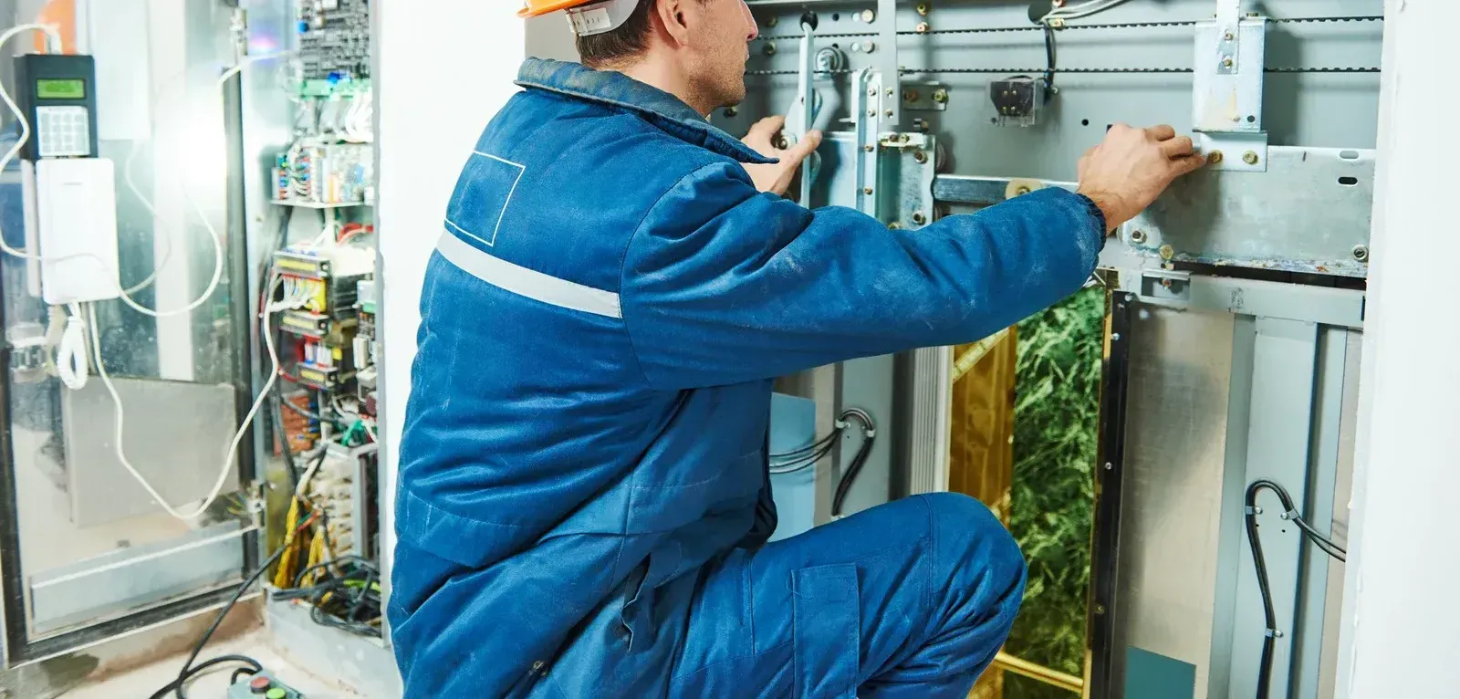 A man in a blue jacket is working on an elevator.