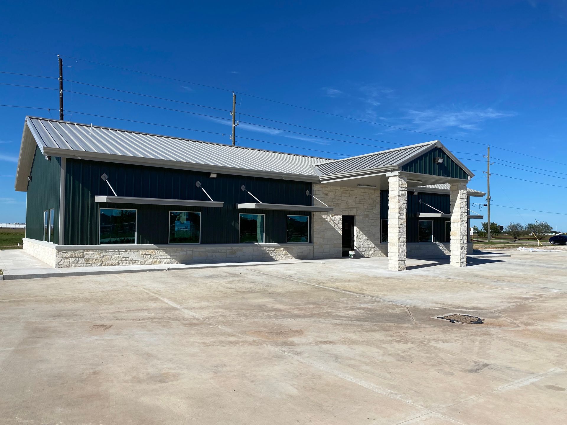 Green and stone building with metal roof under a blue sky, possibly a business or office.