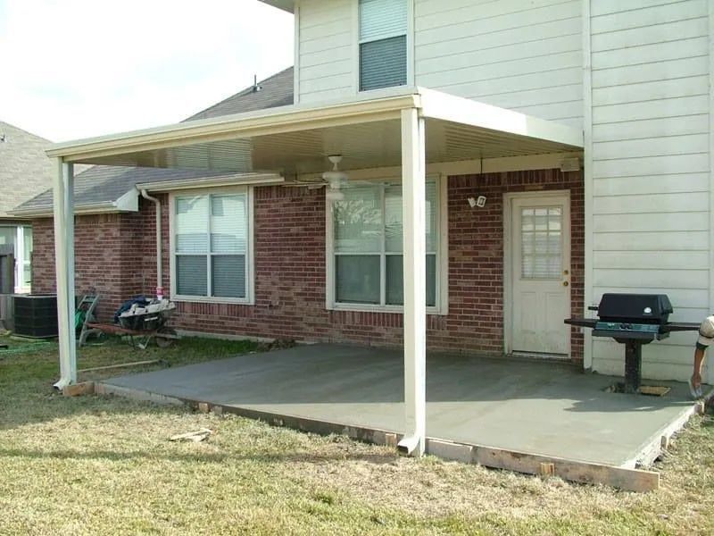 A patio cover attached to a brick home. A grill sits nearby.