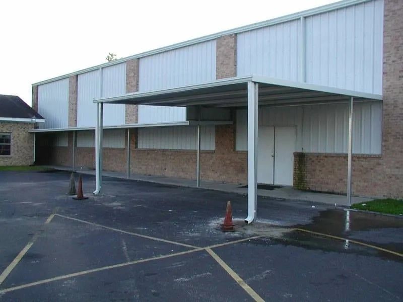 Metal awning over a building's entrance. Brick and metal siding, asphalt parking area.