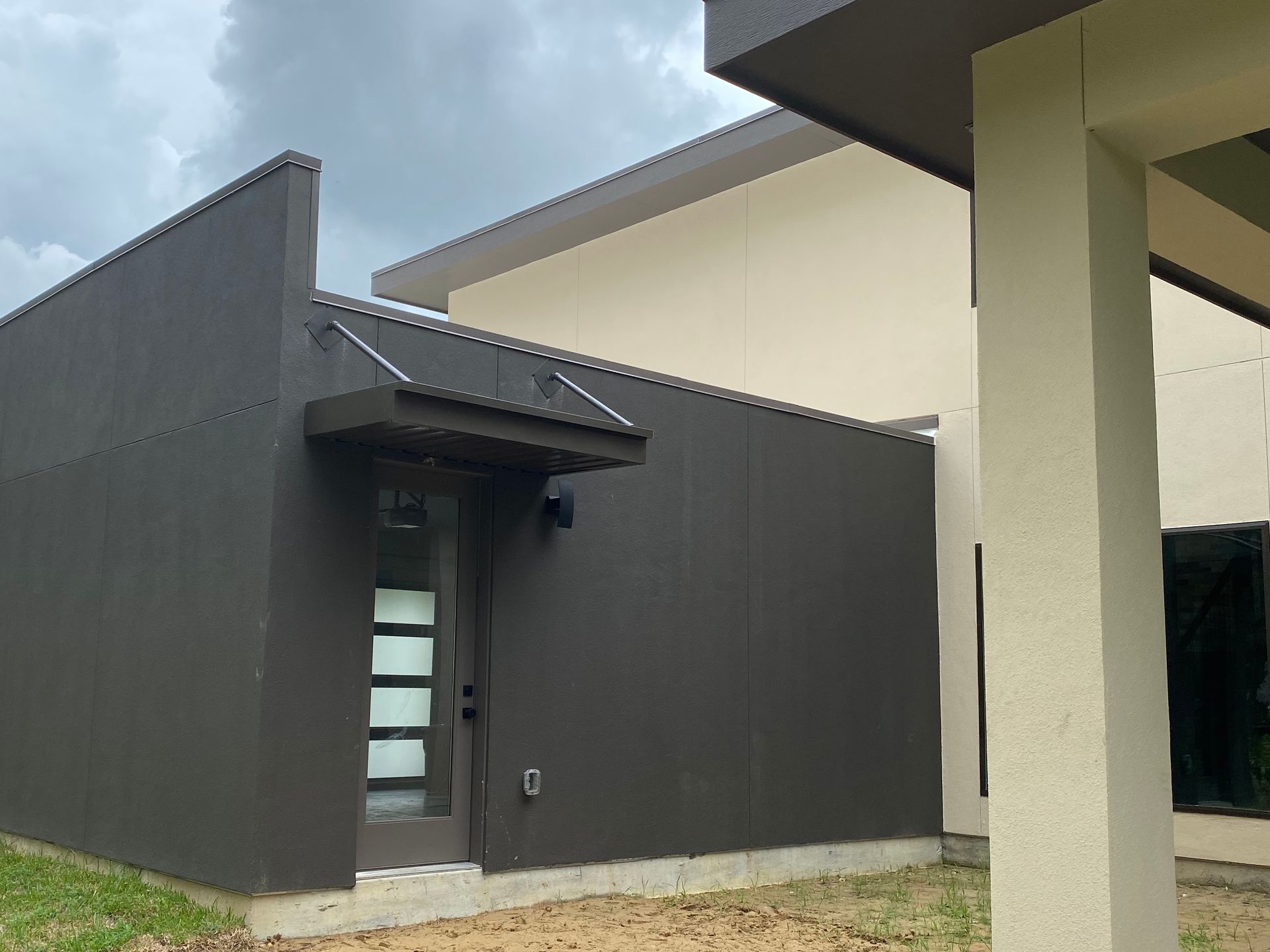 Dark brown building with small overhang over a glass door, next to a beige building with a white column.