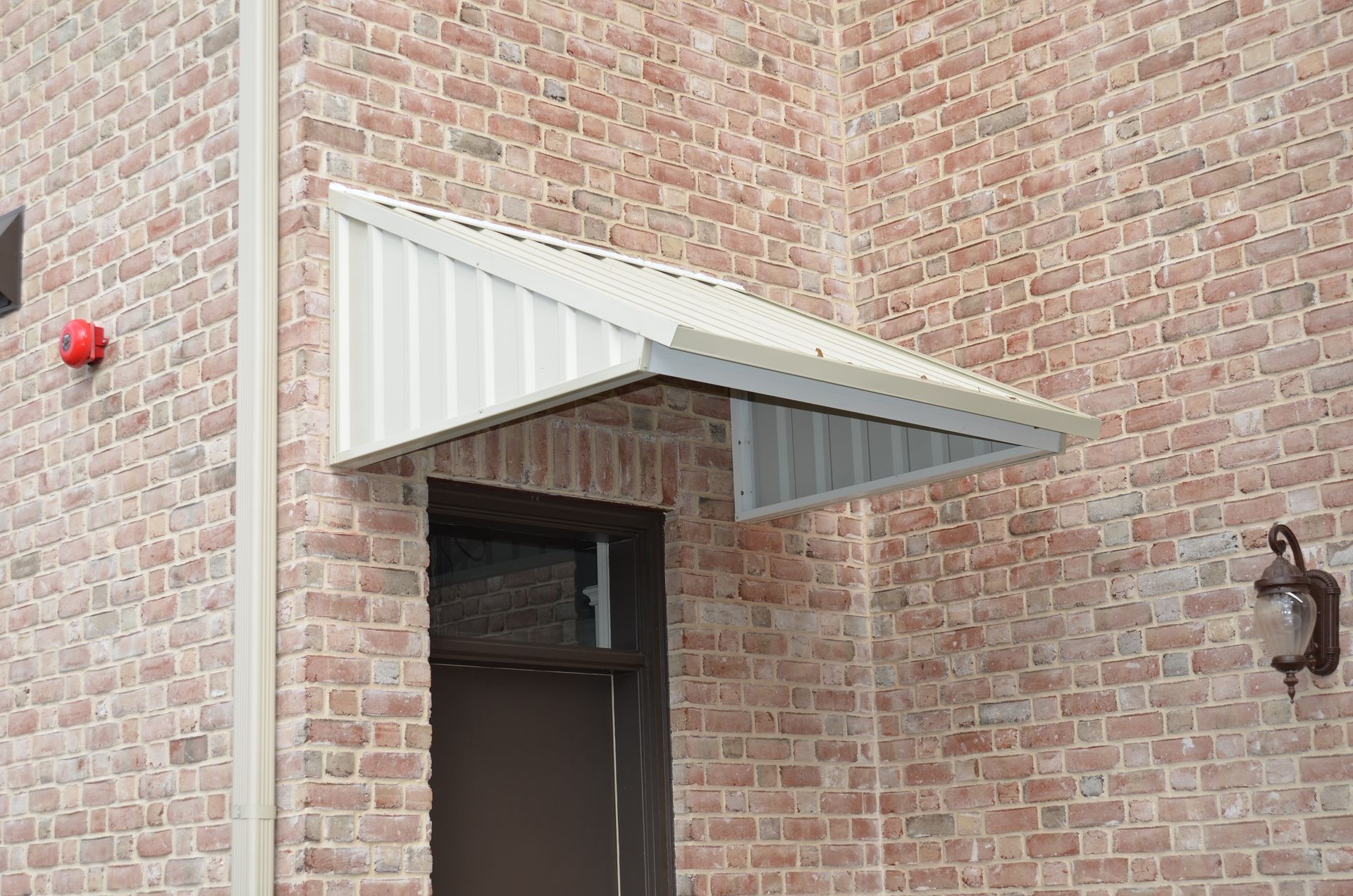 White metal awning over a brown door on a brick building; a red light and lamp are visible.