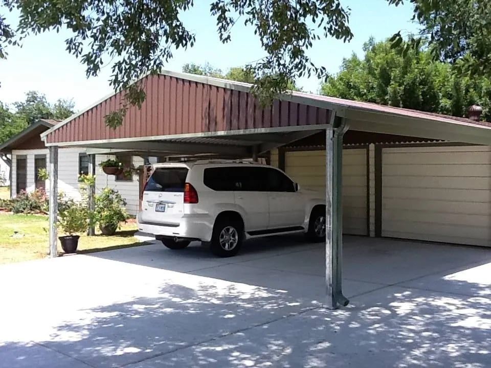 White SUV parked under a carport attached to a two-car garage. Brown and gray roof, concrete driveway.