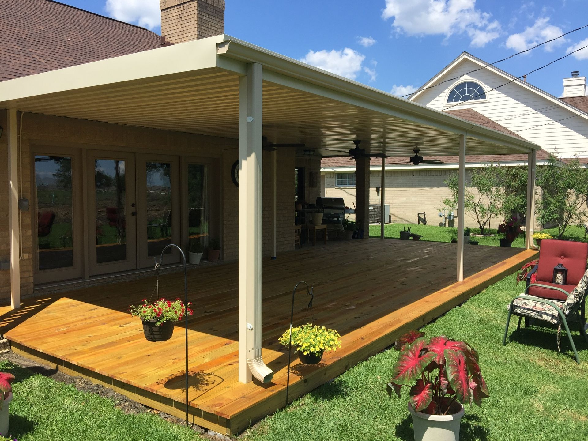 Wooden deck with beige-colored awning, surrounded by grass and a house.