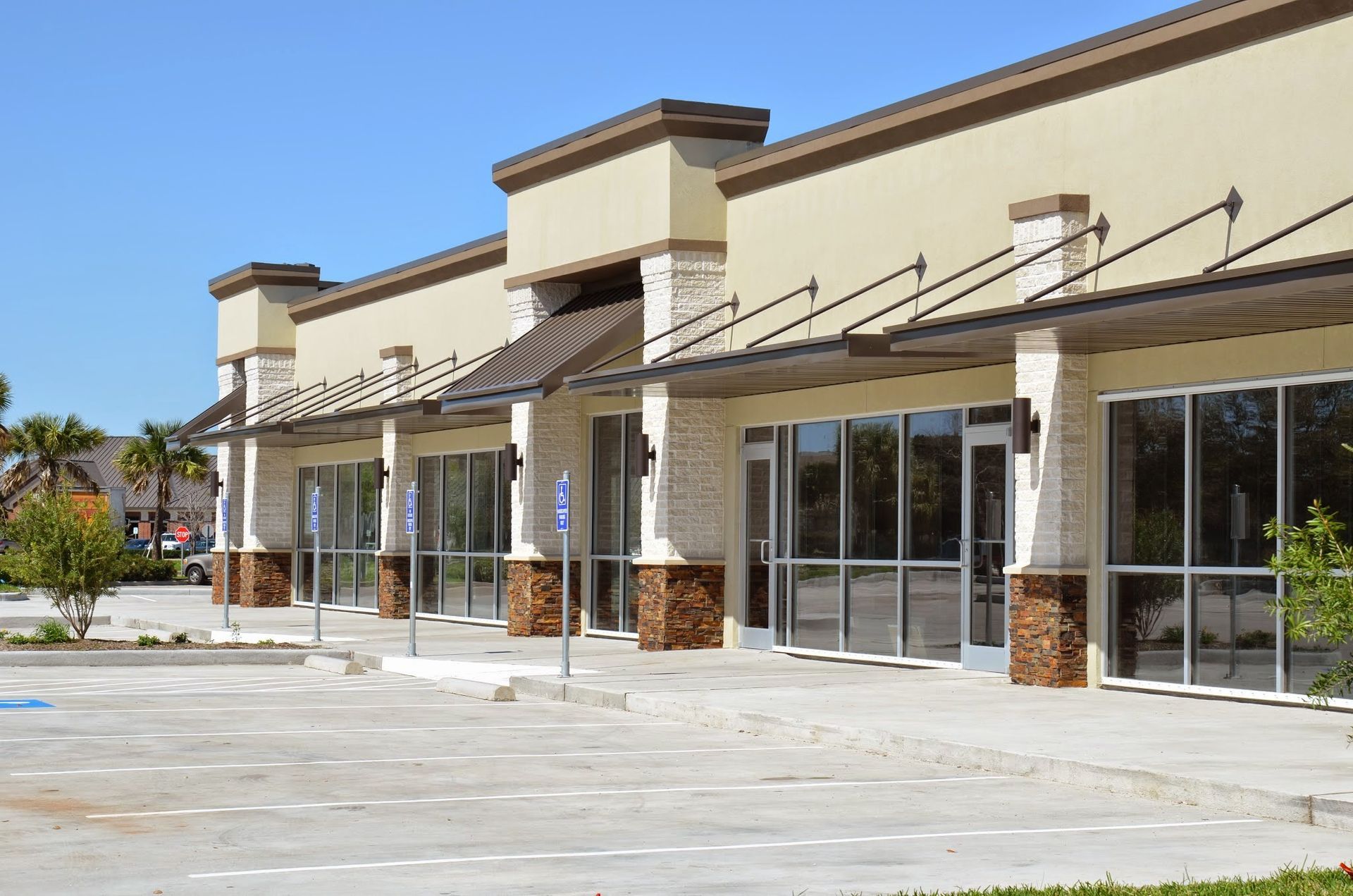 Empty commercial building with parking lot and awnings. Tan facade, stone accents, sunny day.