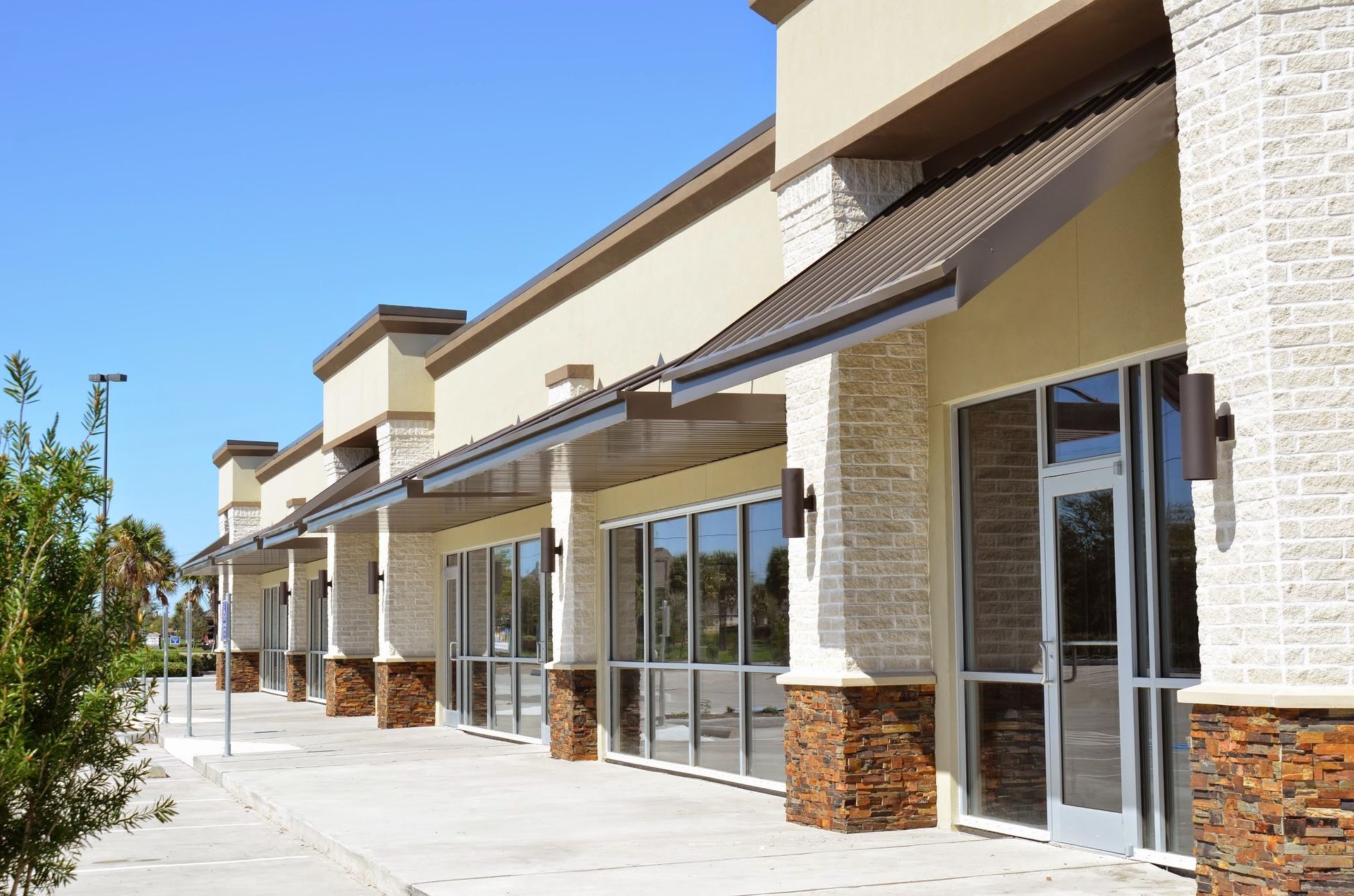 Commercial building with empty storefronts, beige and brick exterior, blue sky.