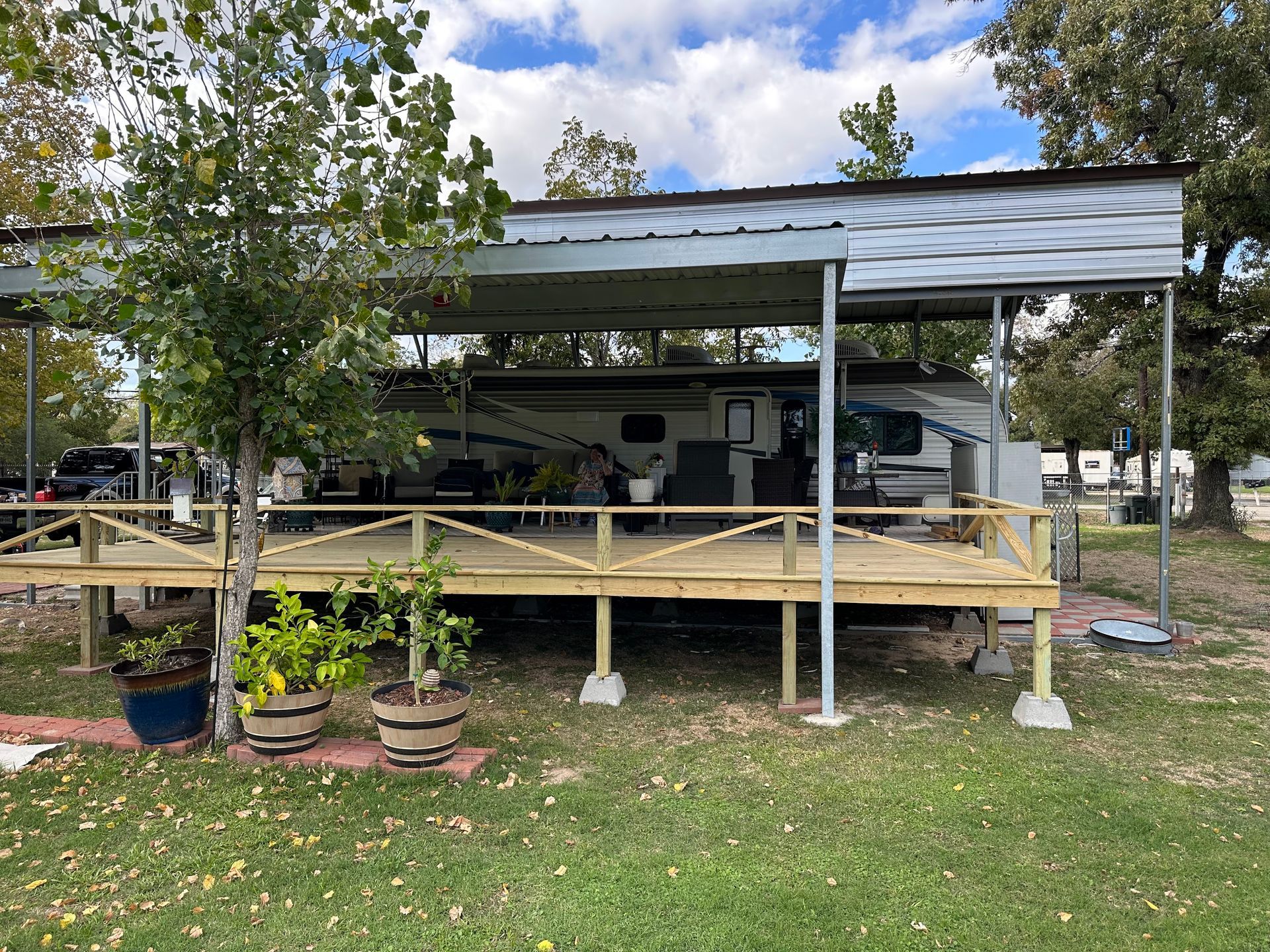 RV parked under a metal carport with a wooden deck.