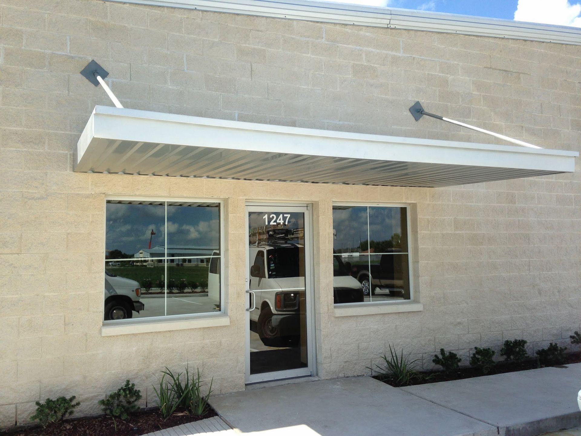Exterior of a tan brick building with an awning over the door and windows.