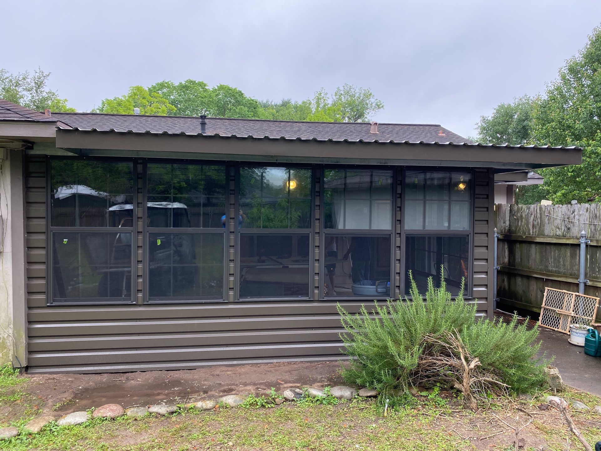A weathered brown building with several large windows, and a shrub in front.