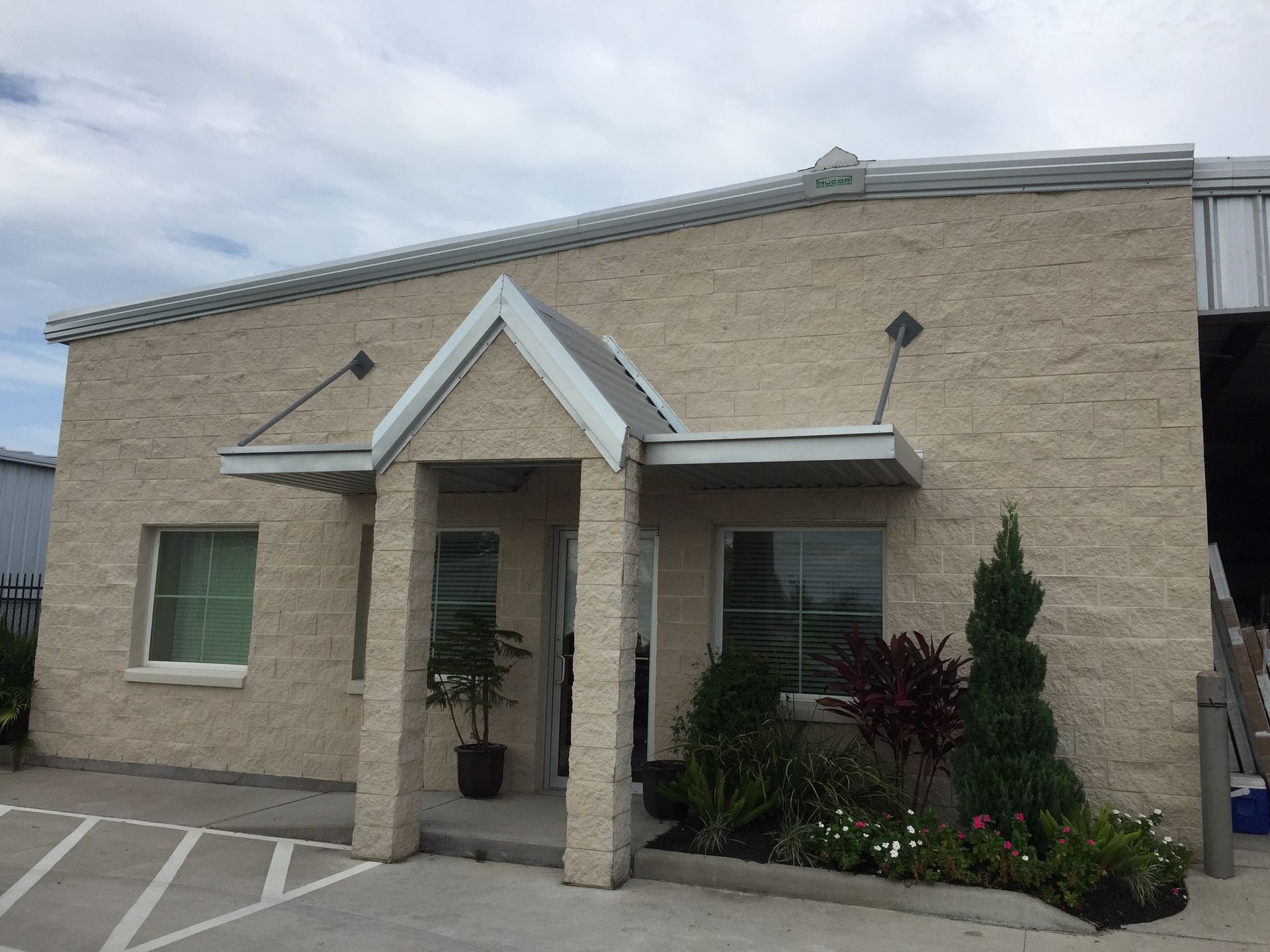 Beige brick building with a covered entryway, windows, and landscaping.