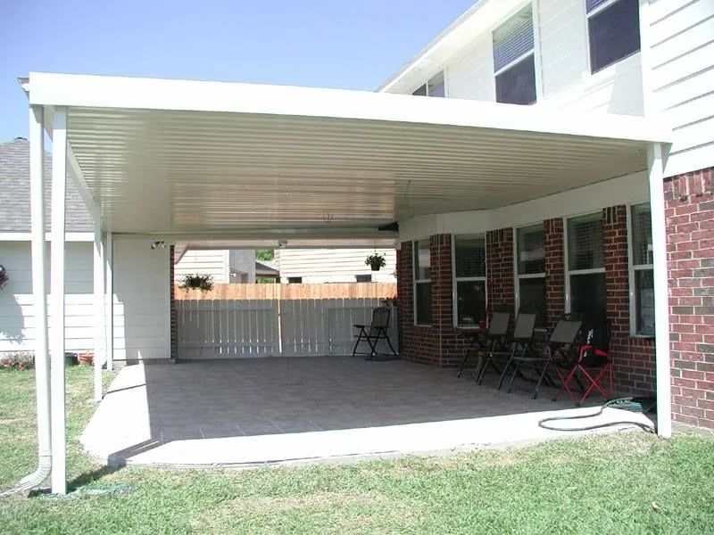 Covered patio attached to a house with brick and siding. Chairs and fence in the background.