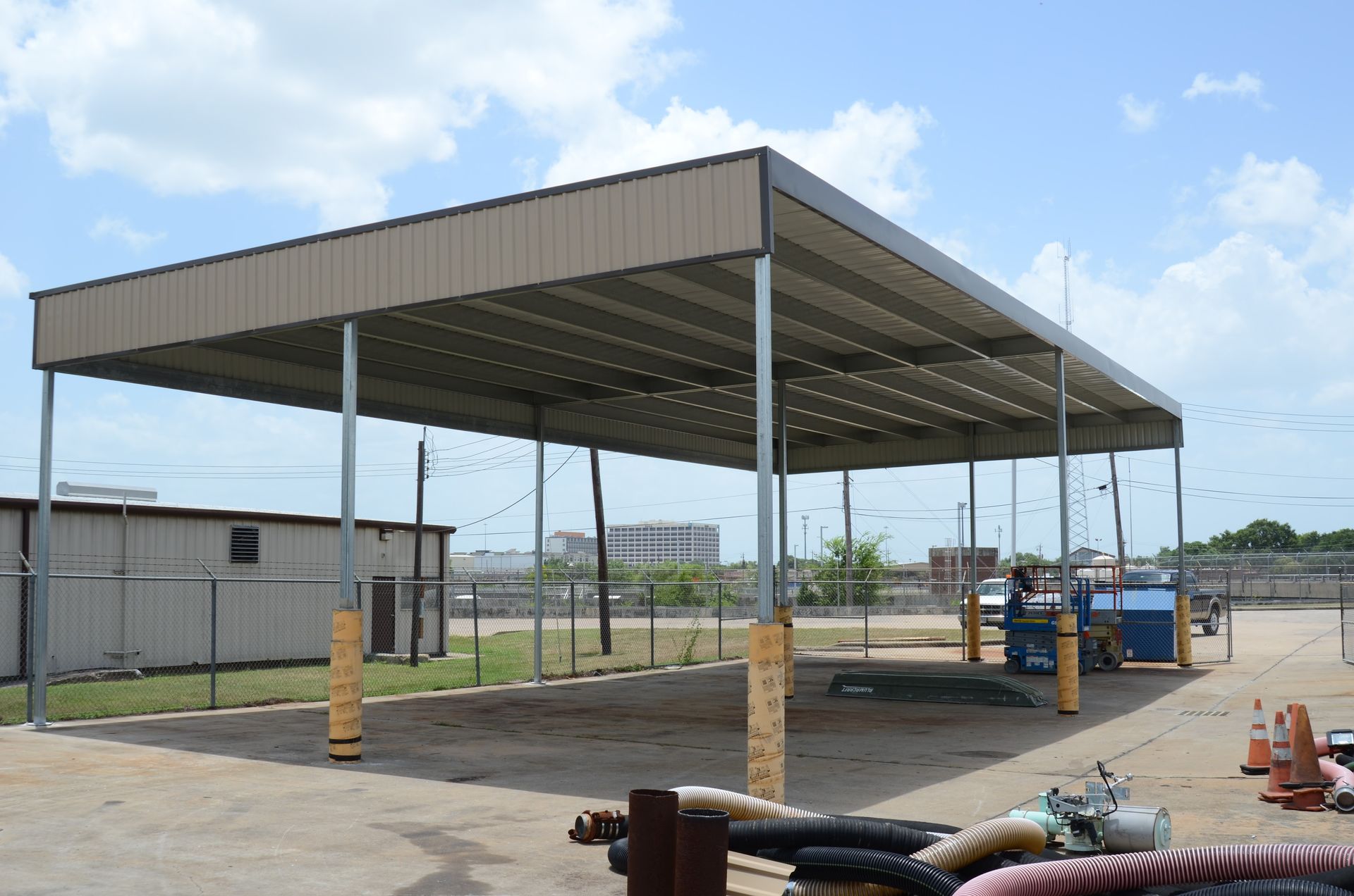 Large metal carport with tan roof, supported by evenly spaced vertical columns, outdoor setting.