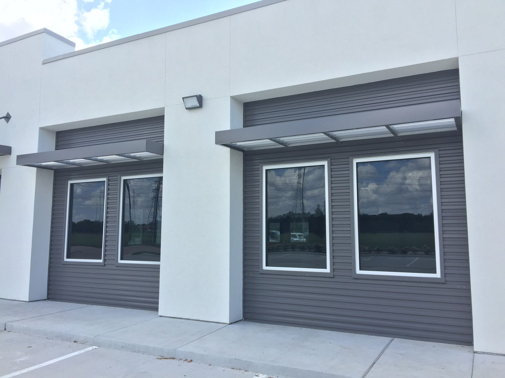 Modern building facade with gray siding, large windows, and awnings.