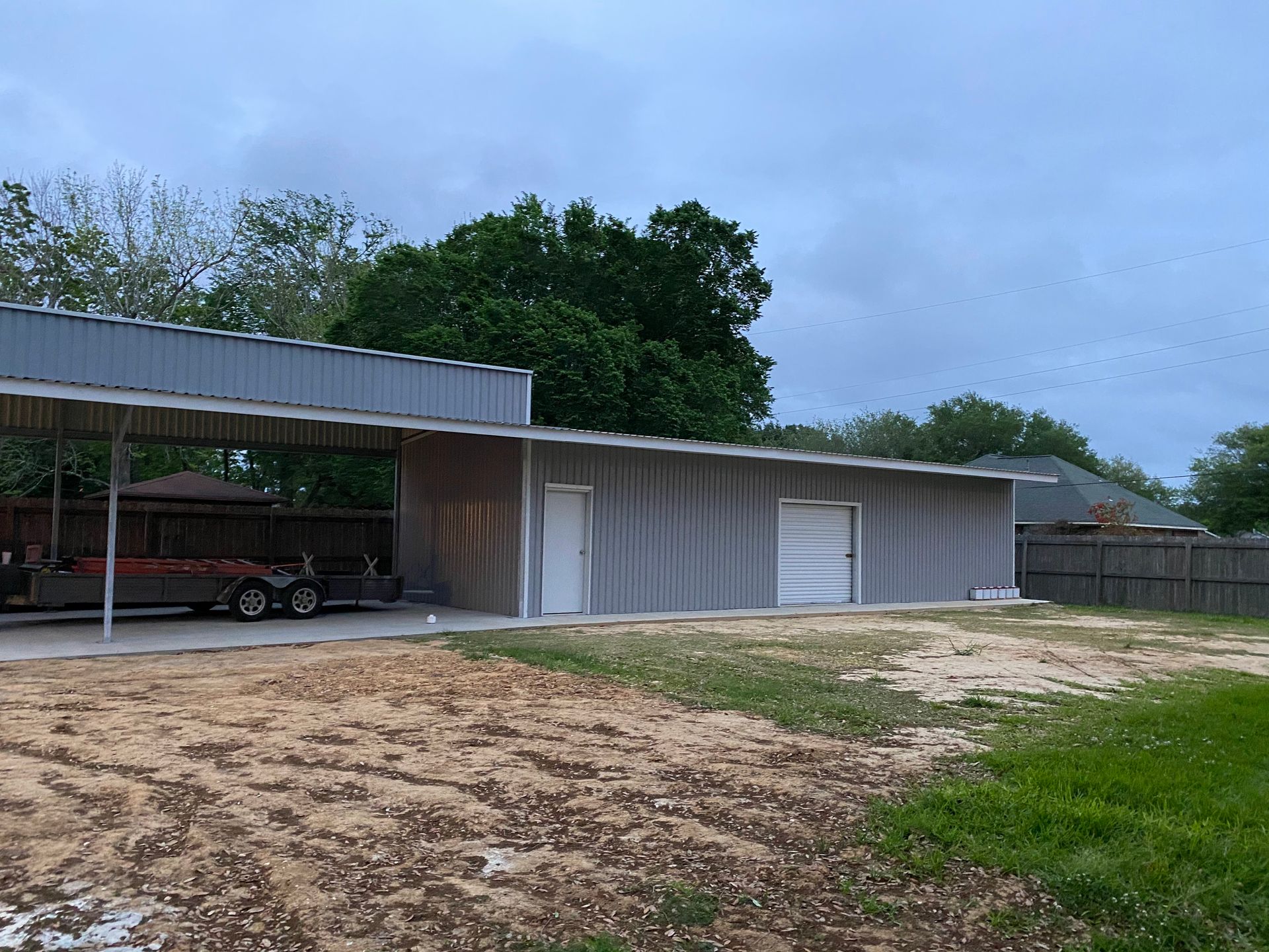 A light-gray metal building with a carport and two doors under an overcast sky.