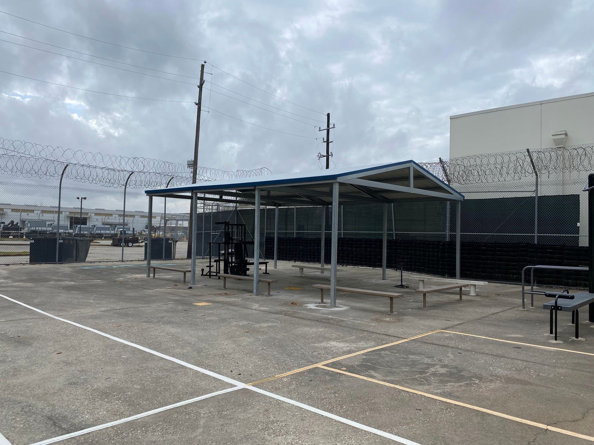 Outdoor gym with covered equipment, surrounded by fences and overcast sky.