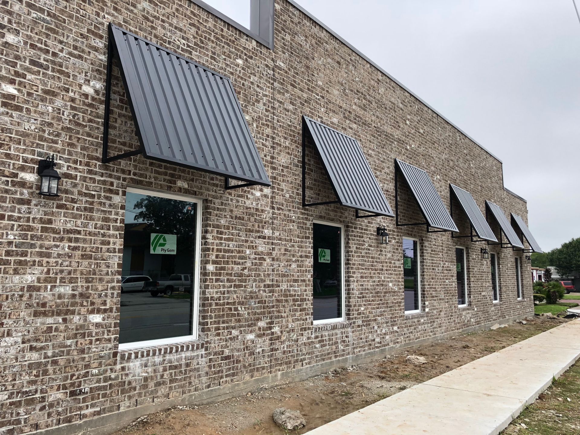 Brick building with black metal awnings over windows and a sidewalk.