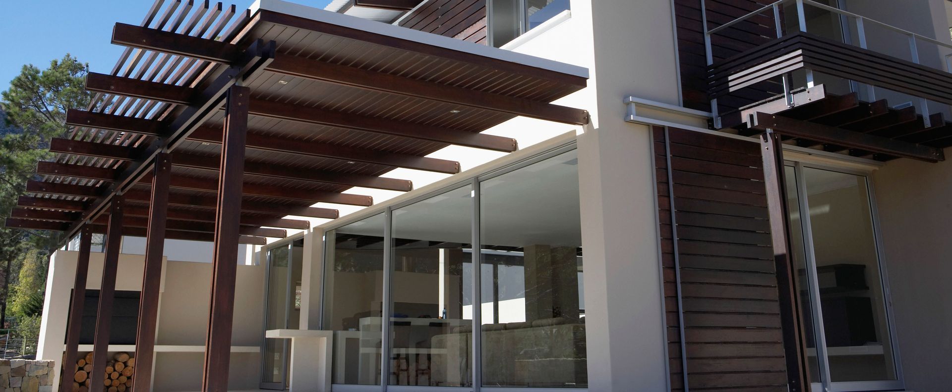 Exterior view of a modern building with a wooden pergola over a glass-walled patio area.