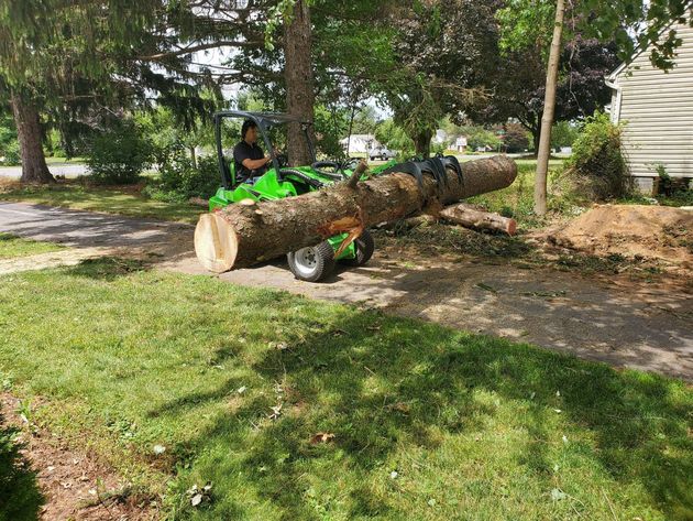 a bulldozer is moving a pile of branches in front of a brick building