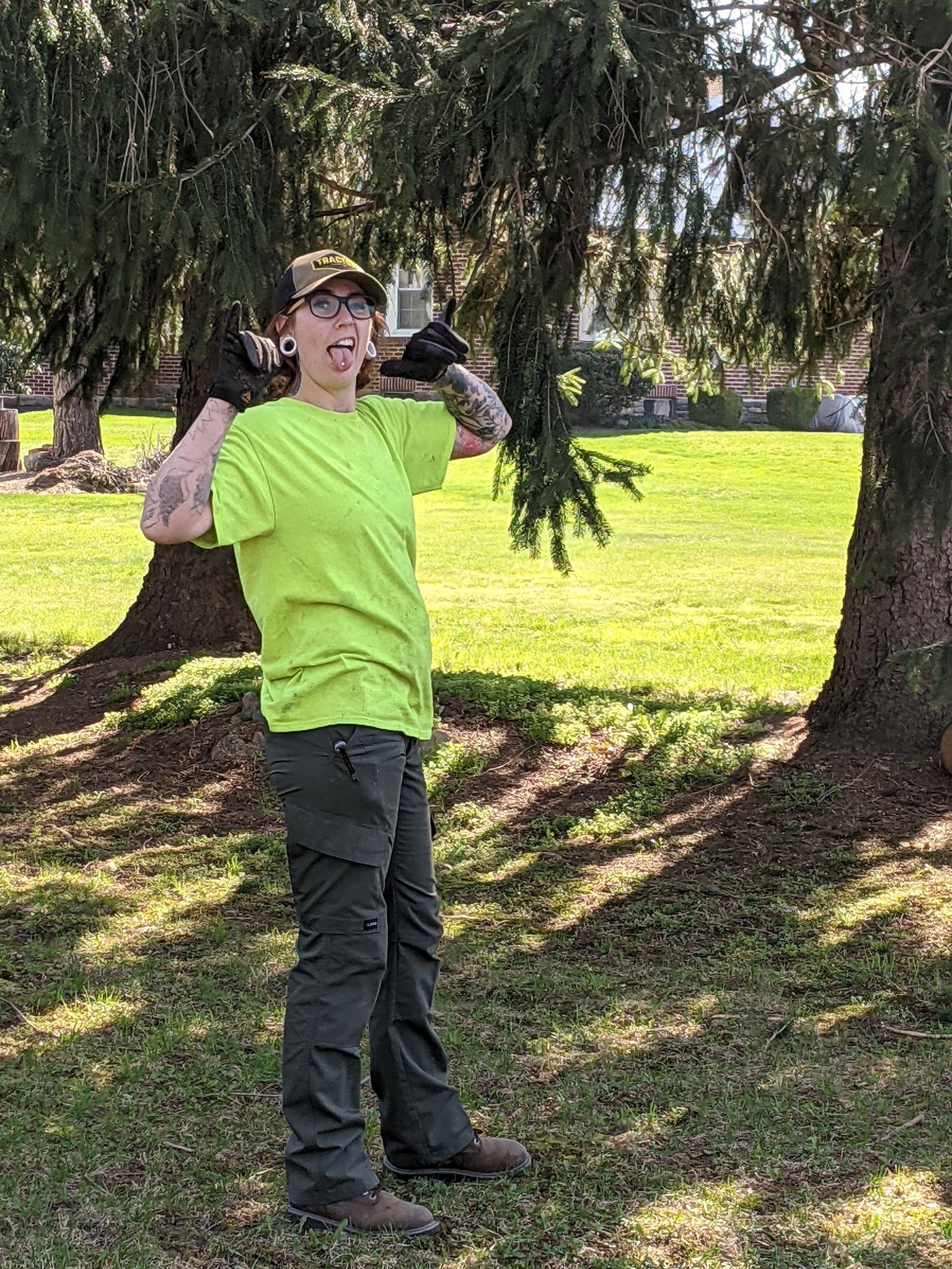 A woman in a yellow shirt is standing in a park next to a tree.