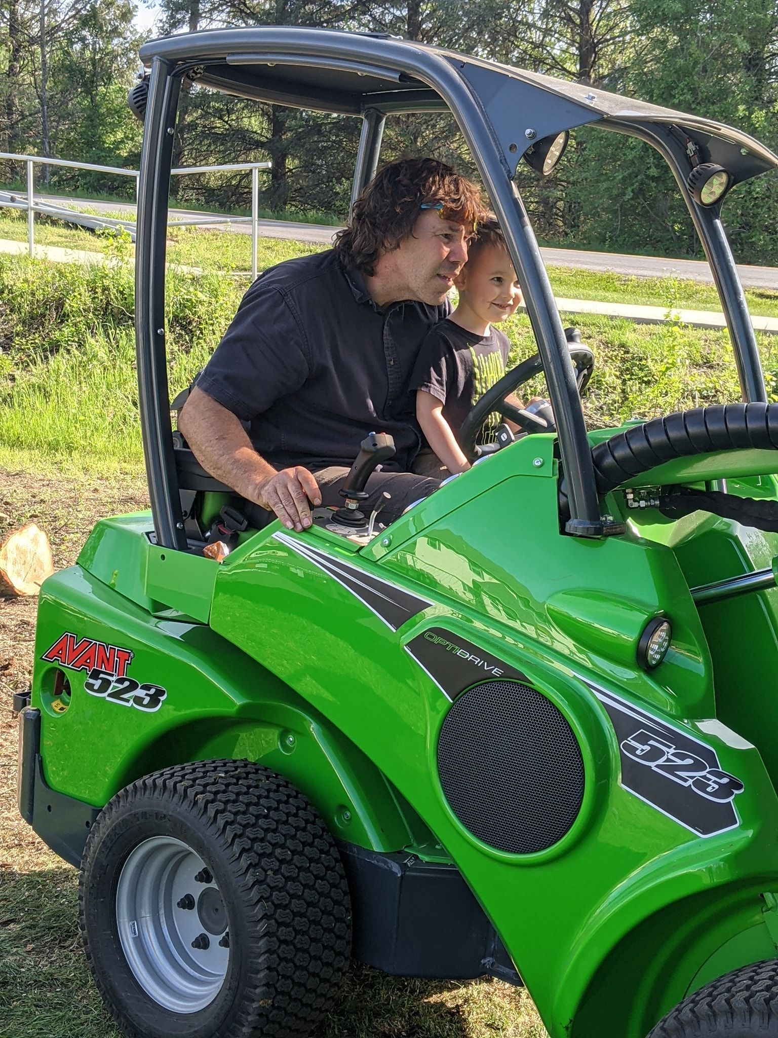 A man and a child are riding a green tractor.