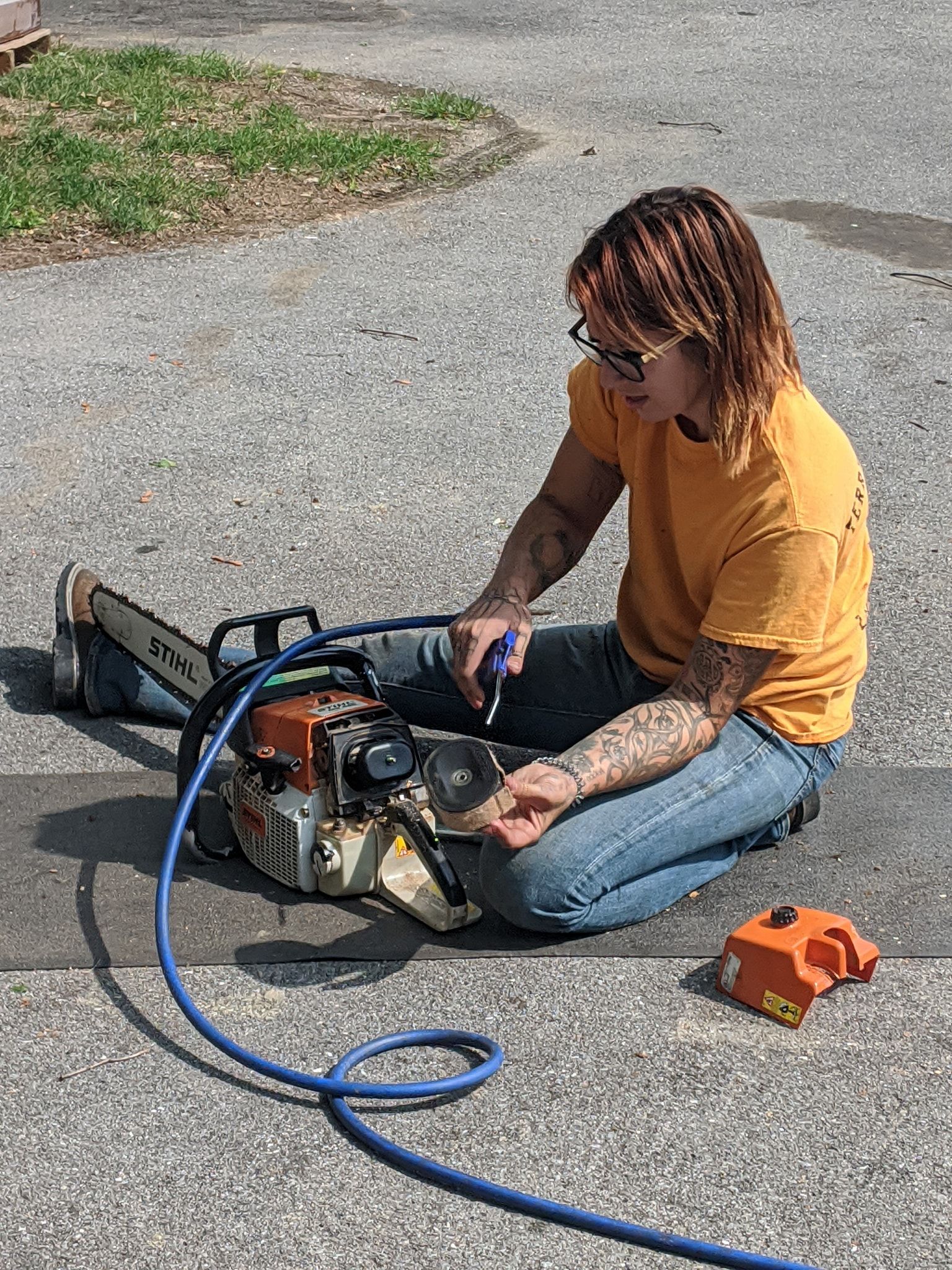 A man is sitting on the ground fixing a chainsaw.
