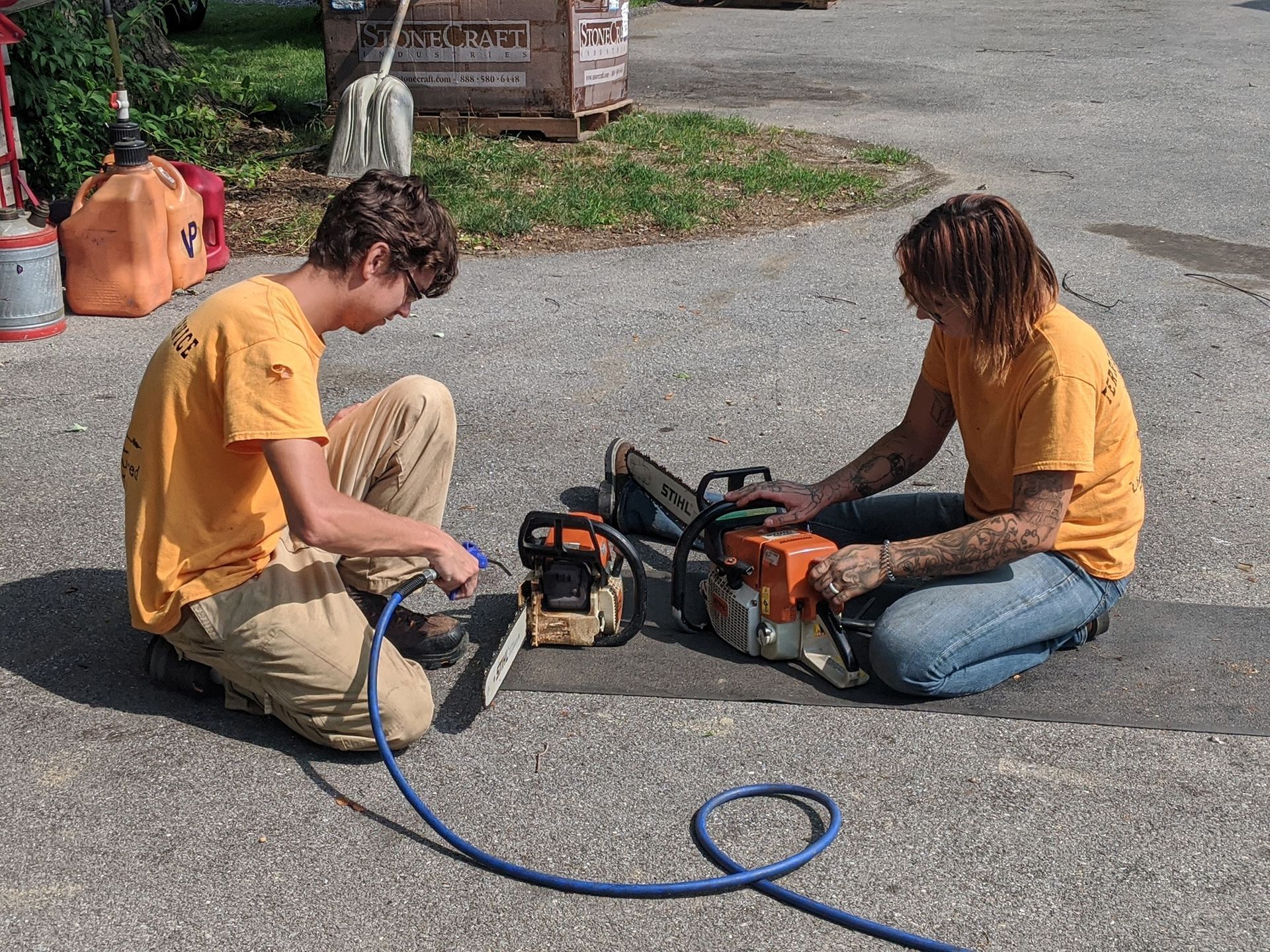 Two people are sitting on the ground working on chainsaws