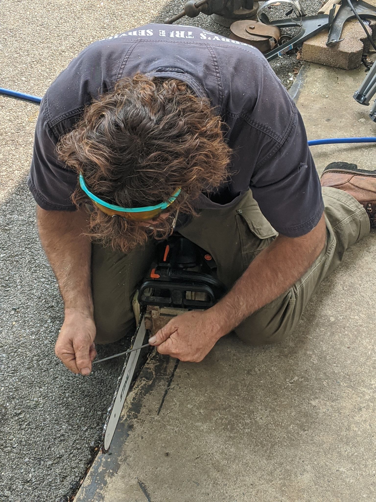 A man is kneeling down on the ground using a chainsaw.