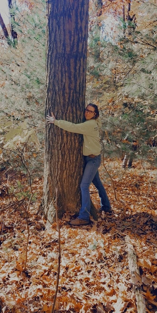 A woman is hugging a large tree in the woods.