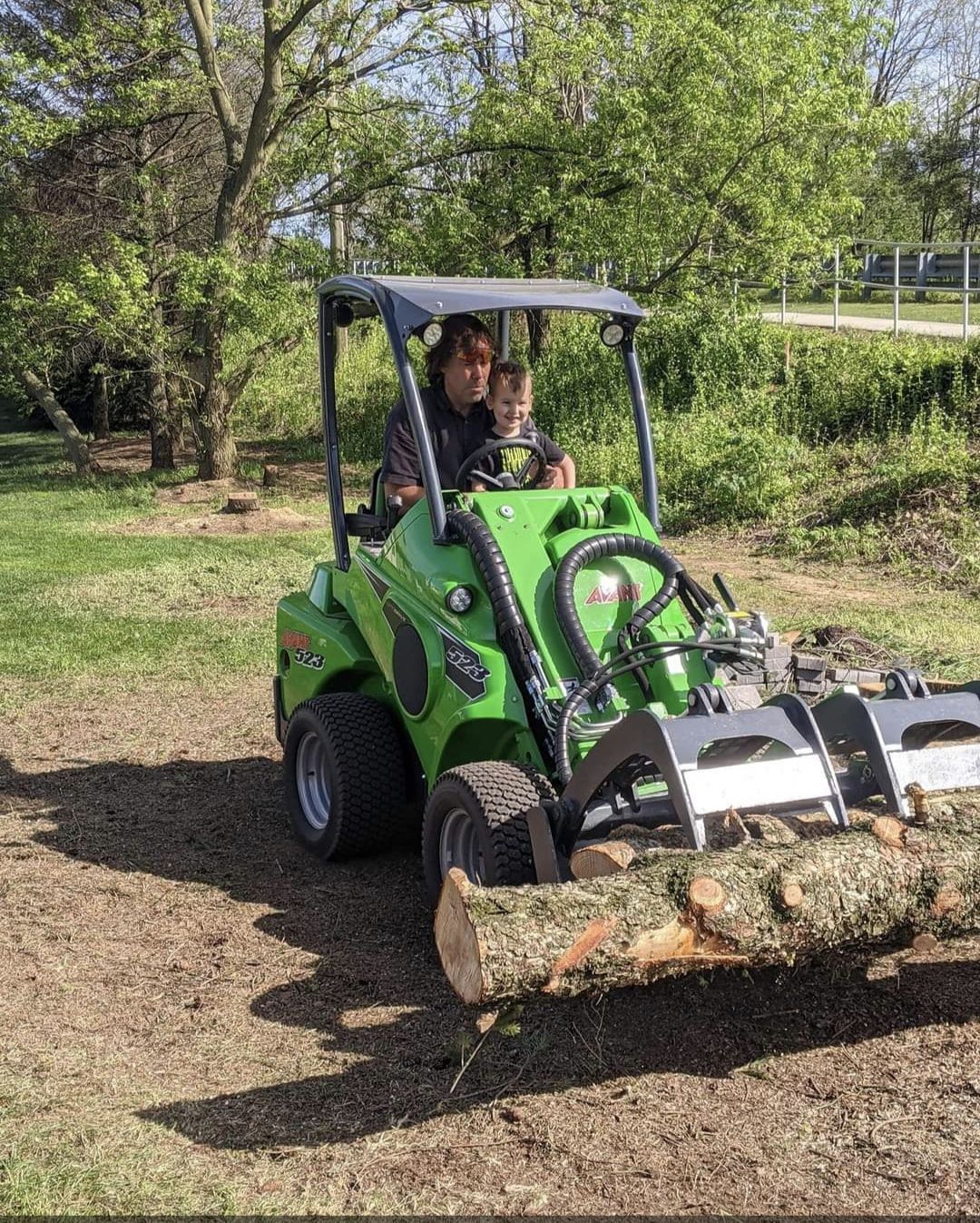 A man is driving a green tractor carrying a large log.