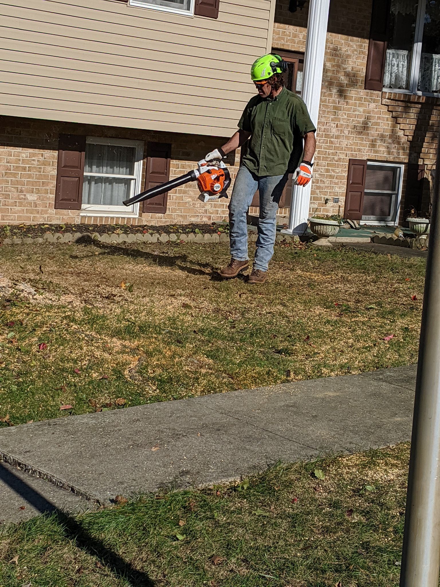 A man is standing in front of a house using a lawn mower.