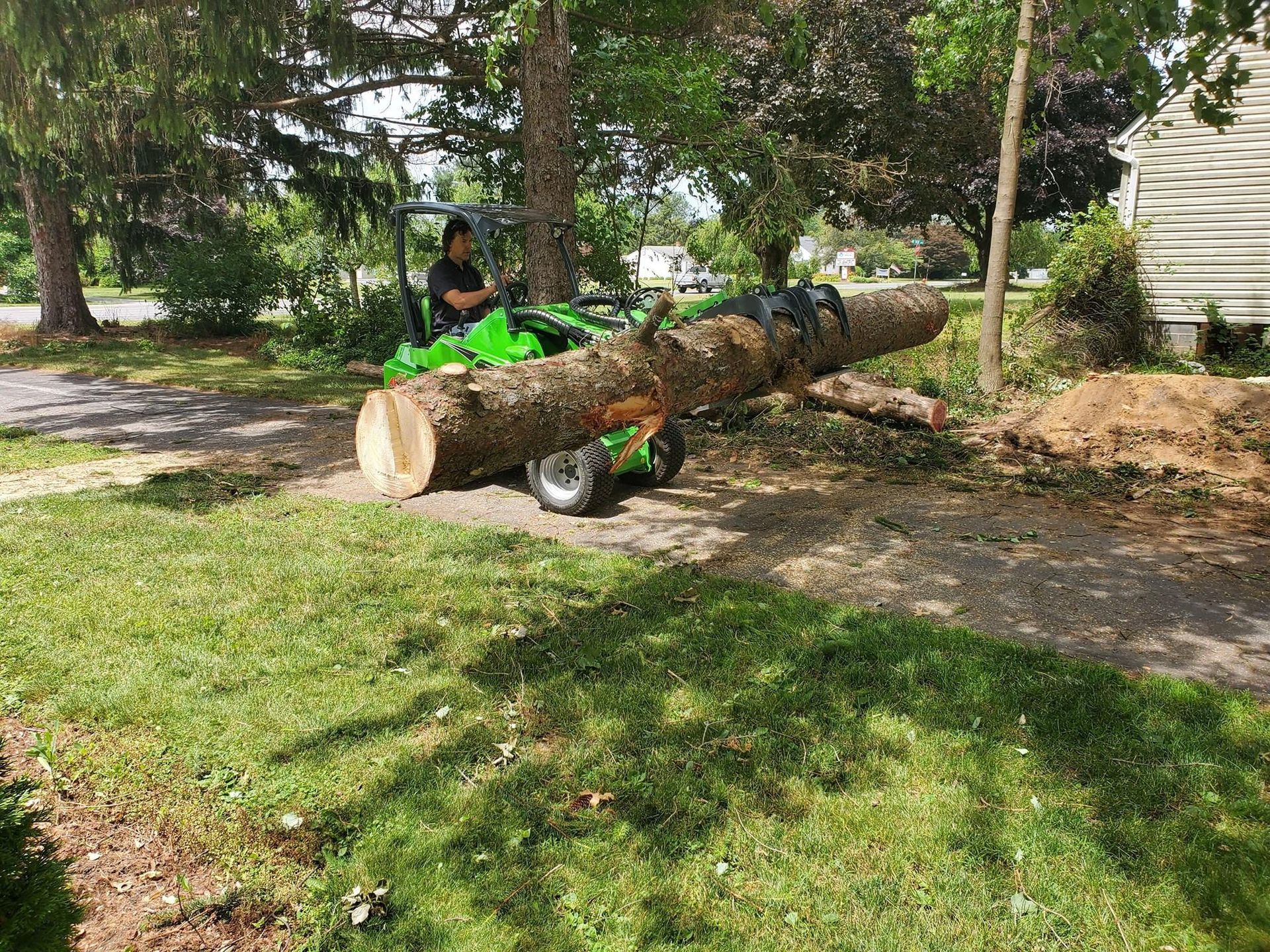 A green tractor is carrying a large log in a yard.